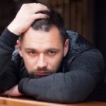 Hombre pensativo con barba y chaqueta negra apoyado en una mesa, reflexionando sobre las razones por las que no se enamora.