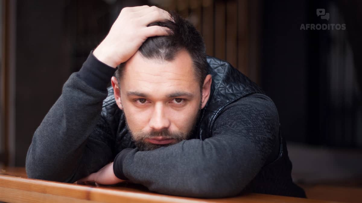 Hombre pensativo con barba y chaqueta negra apoyado en una mesa, reflexionando sobre las razones por las que no se enamora.