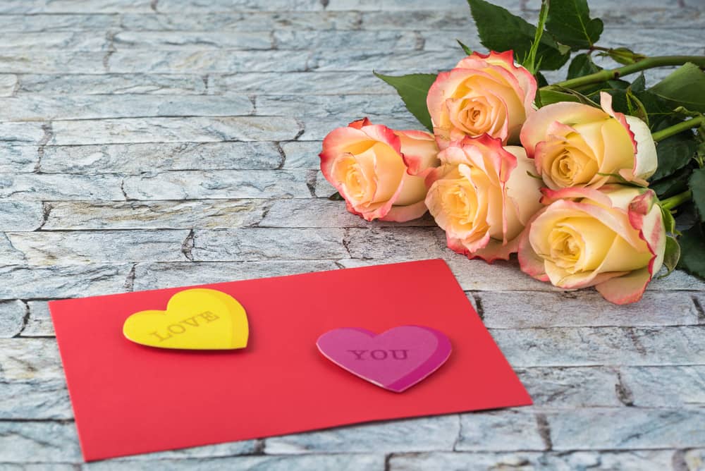 Tarjeta roja con corazones que dicen "Te amo" y rosas amarillas.